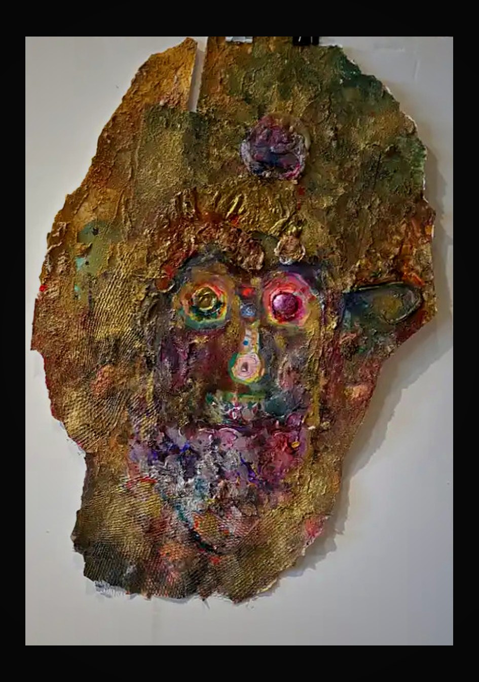 Primordial face emerging from layered gold leaf and iridescent pigments on irregular paper