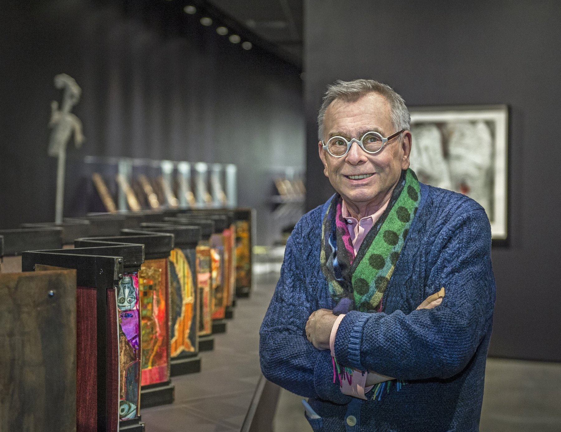 William Harper standing confidently in his gallery exhibition with illuminated enamel artwork behind him